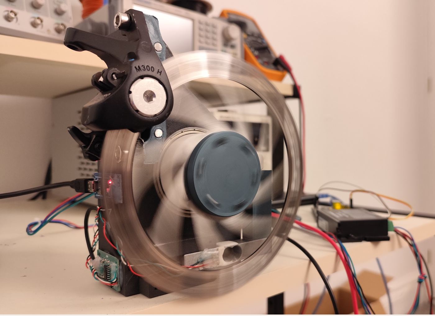 A brake disc spinning in a blur on the motor characterisation rig, with a caliper load and bench instruments behind